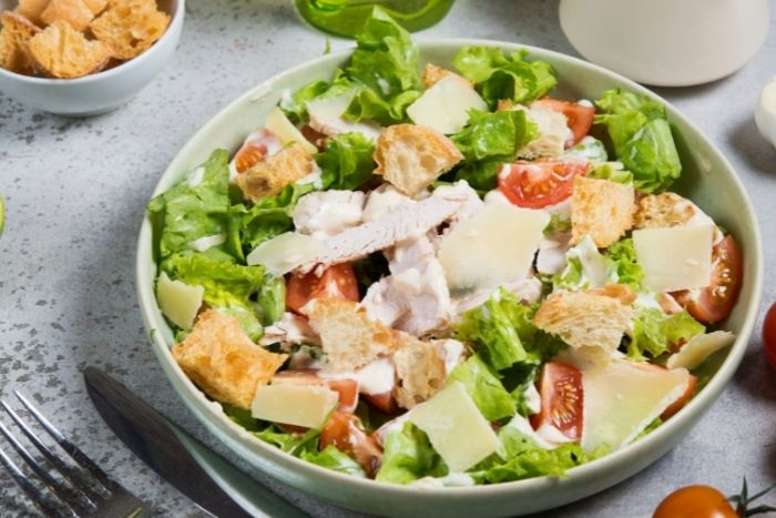 A bowl of salad with lettuce, croutons, shaved parmesan and tomatoes