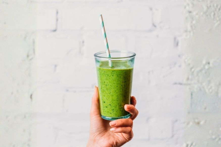 A woman's hand holding a green smoothie in a glass with a straw